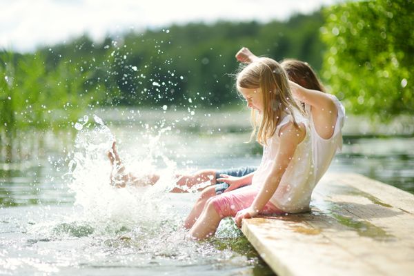 2 Kinder sitzen auf einem Steg am Wasser