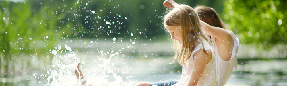 2 Kinder sitzen auf einem Steg am Wasser