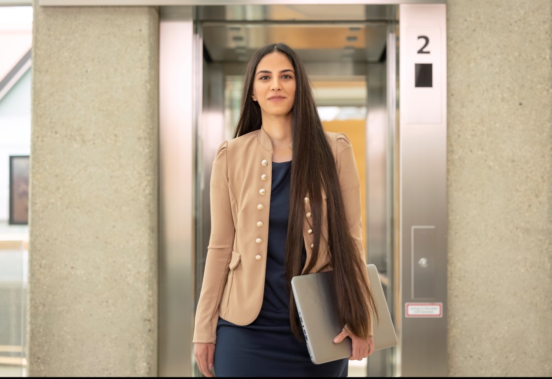 Mitarbeiterin mit Laptop steigt aus dem Lift aus