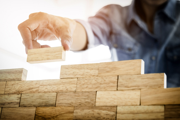 Hand of engineer playing a blocks wood tower game (jenga) on blueprint or architectural project concept.